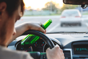 Drunk young man driving a car with a bottle of beer.