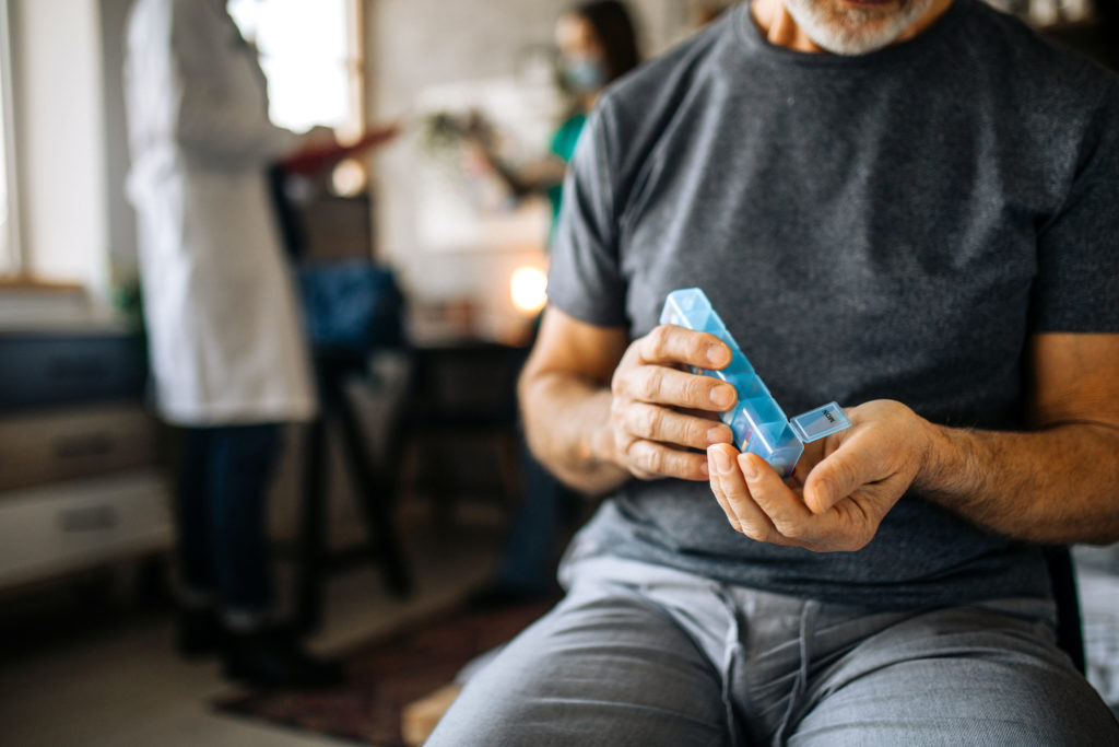 Senior man at home taking medications from a daily pill organizer box