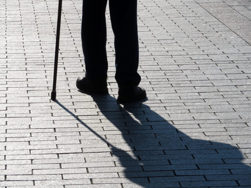 Silhouette of man walking with a cane, long shadow on pavement