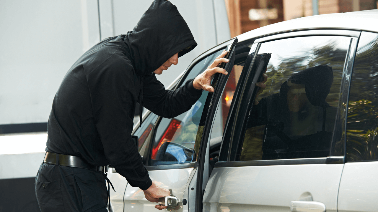 A man opening a car and stealing personal items.