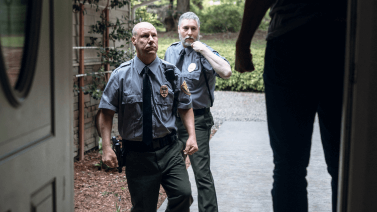 Two police officers approaching a man in his doorway.